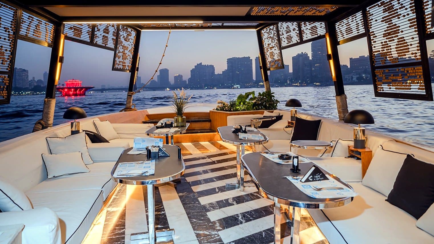 The lounge deck of the dinner boat at dusk, with the Cairo skyline across the Nile